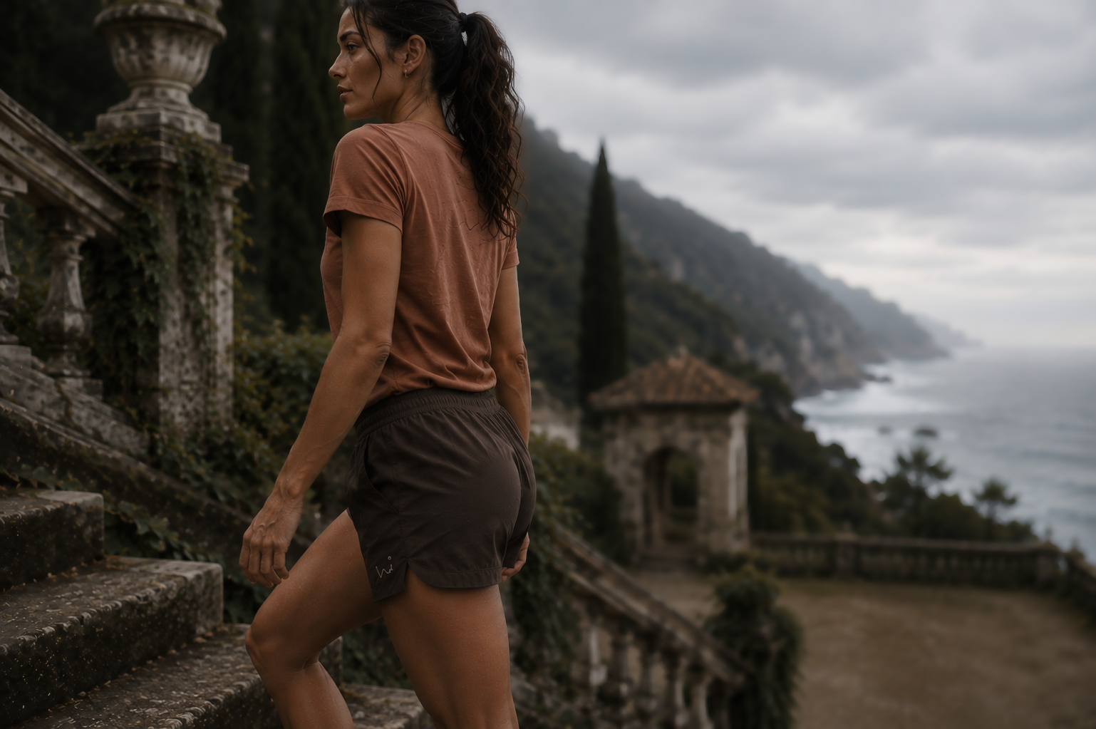 A woman climbing coastal stone steps in a terracotta tee